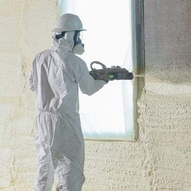 Person in safety gear spaying a wall with spray foam