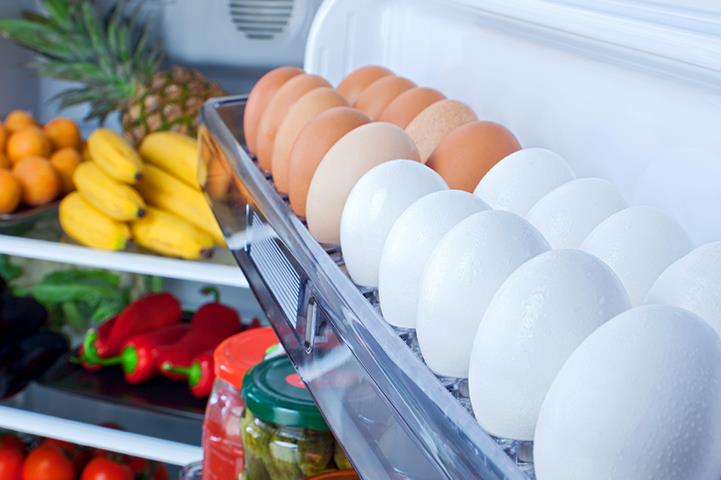 open refrigerator with eggs in the door and bananas pineapple eggplant peppers tomatoes oranges