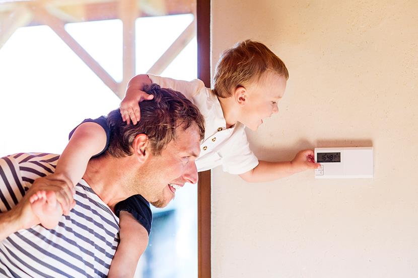 man holding toddler on shoulders leaning over to touch thermostat on wall 1 3 2 11