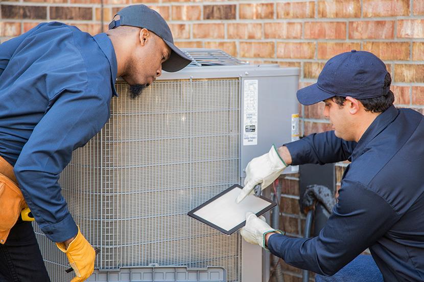 two men net to exterior air conditioning heat pump system one man holding a tablet and the other man