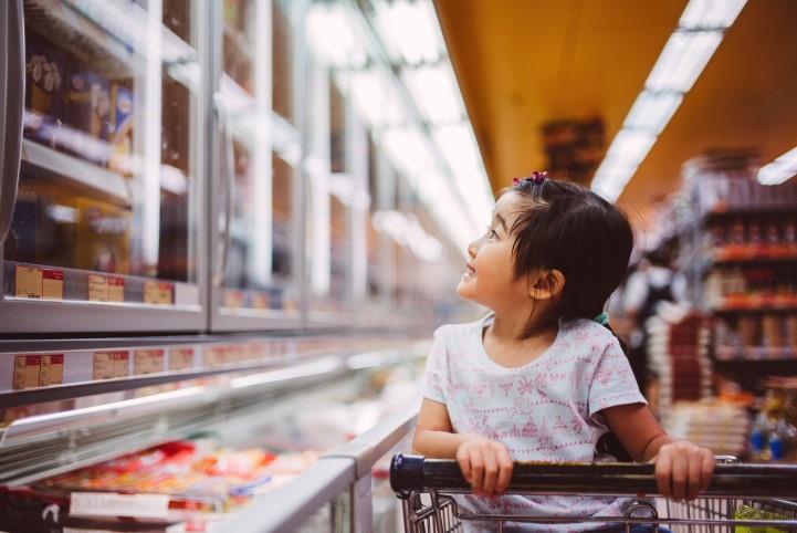child in shoopping cart looking at refrigerated section