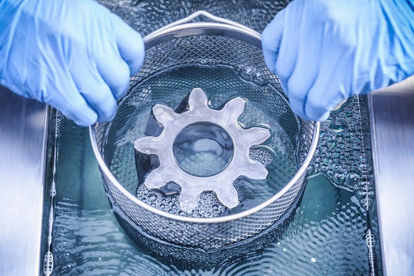 person wearing gloves cleaning metal item in an ultrasonic cleaner