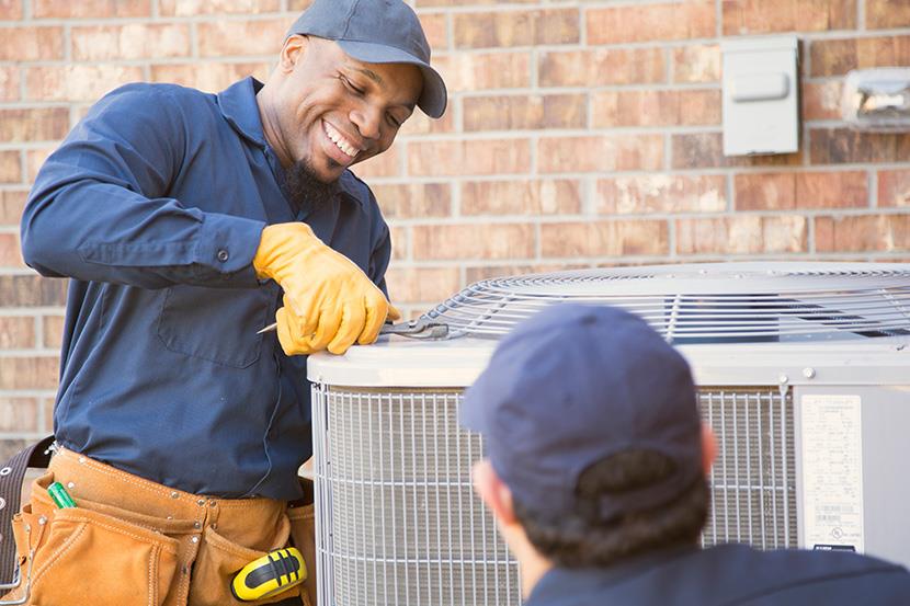 two men working on an air conditioning unit outside