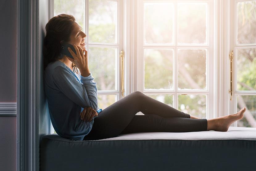 woman sitting on window seat and talking on the phone