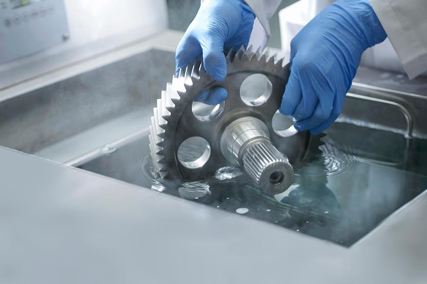 worker wearing blue gloves holding gear in cleaning liquid
